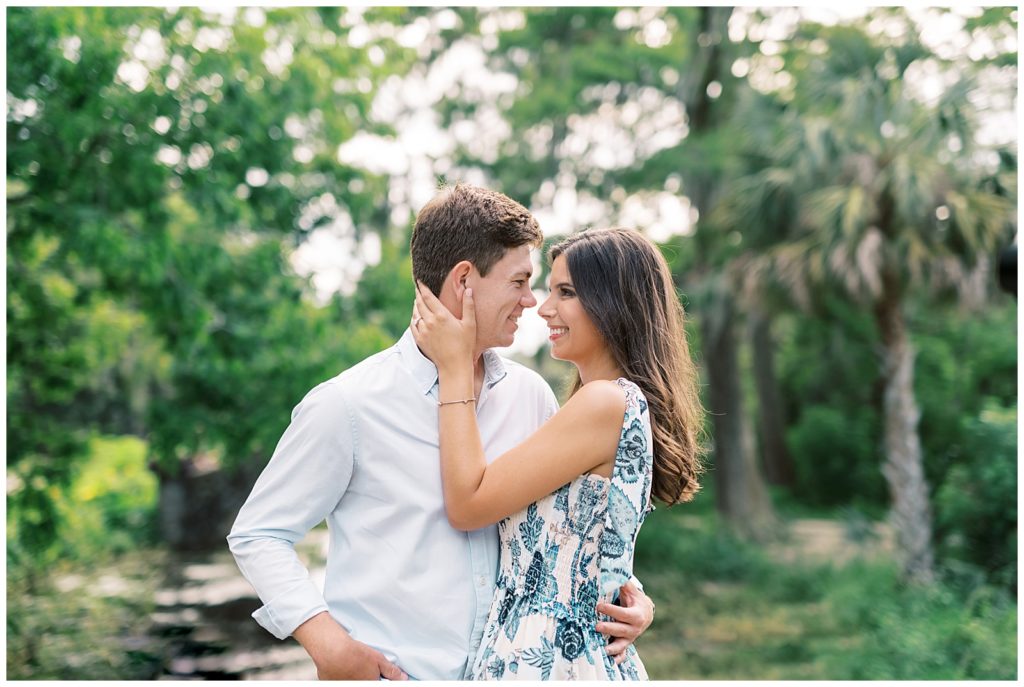 A couple wearing a white shirt and a blue dress take engagement pictures in City Park of New Orleans under the large live oak trees over the stone bridge on the lake