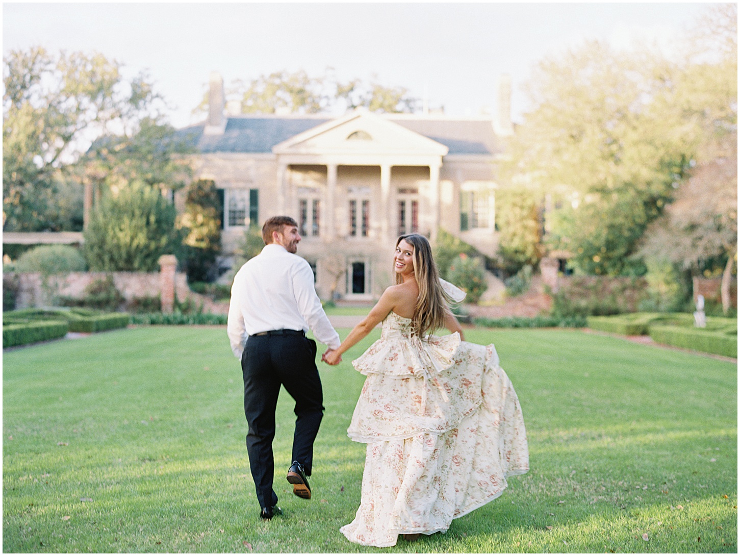 Couple wearing a suit and long dress run through open field during sunset at Longue Vue House and Gardens engagement session in New Orleans, Louisiana